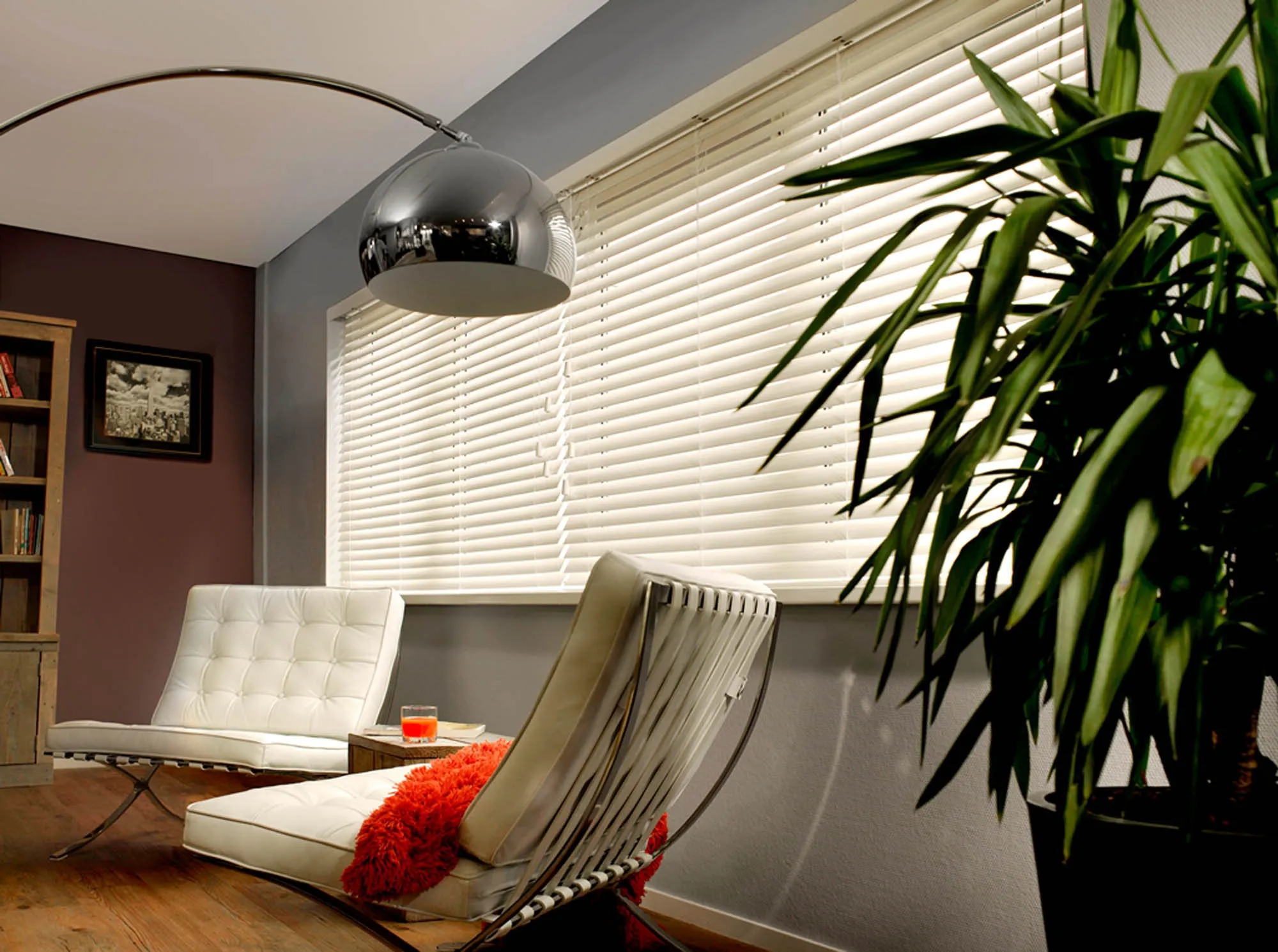 Cream venetian blinds behind a white leather lounge chair